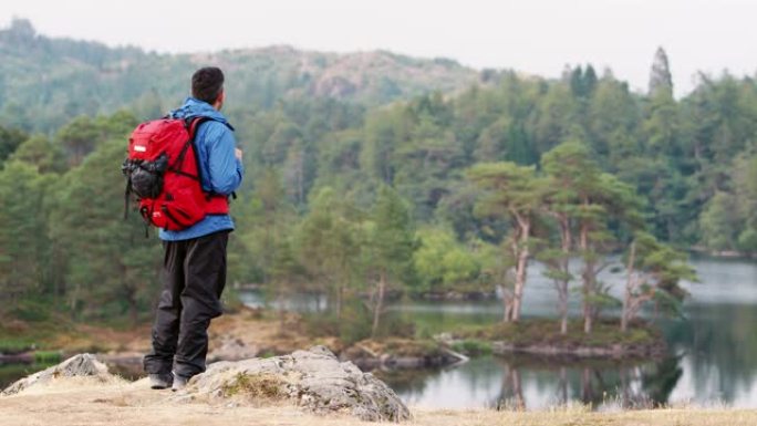 白人成年男子站在山上欣赏湖景，英国湖区后景