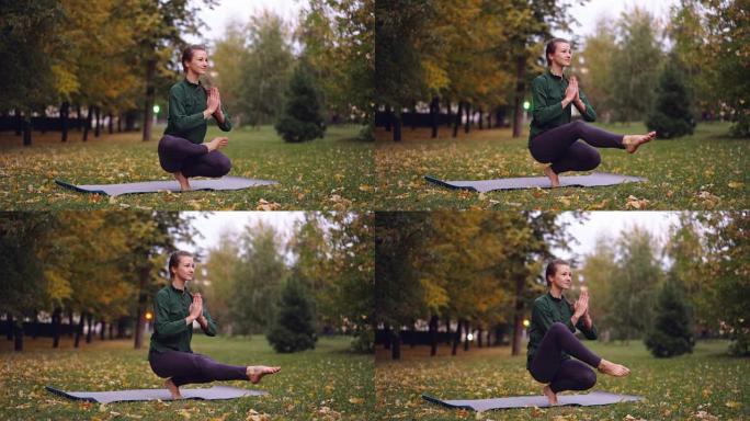 美丽的女孩yogini正在公园的垫子上练习，练习一条腿的平衡姿势并放松。健康的生活方式、自由时间活动