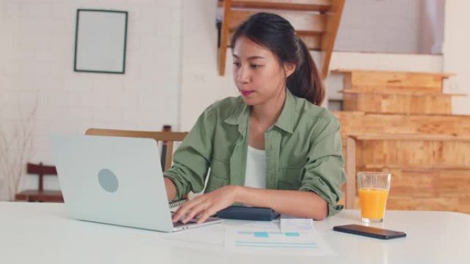 商业亚洲女性使用笔记本电脑记录在厨房工作的收入和支出。