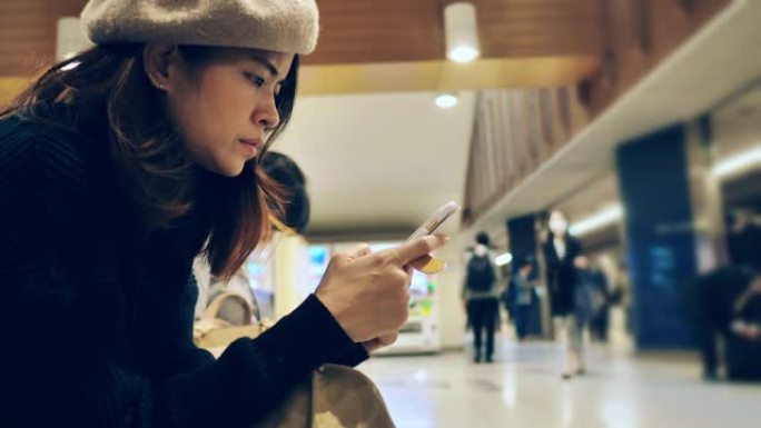 等待火车和使用智能手机的亚洲女性游客。
