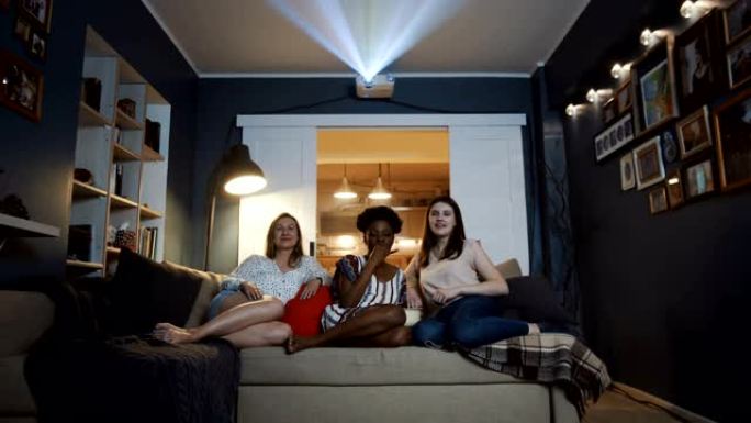 快乐美丽的多民族女性朋友在家里用投影仪慢动作一起看最喜欢的电视剧。