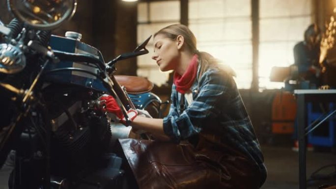 年轻漂亮的女机械师正在设计一辆定制的Bobber摩托车。穿着方格衬衫和围裙的才华横溢的女孩。她转身对