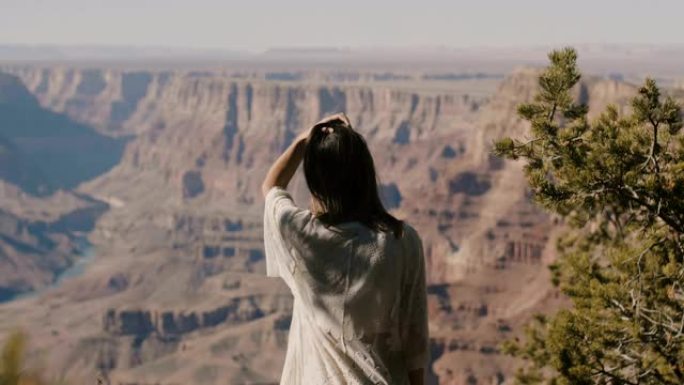 回顾年轻快乐的旅游女人抚摸头发，观看令人难以置信的大峡谷沙漠山脉风景。