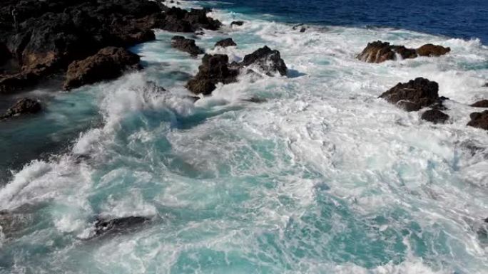 神话般的海上冲浪。在暴风雨中，海浪袭击黑色岩石时，在蓝色和碧绿的水上飞行。空中射击，4K