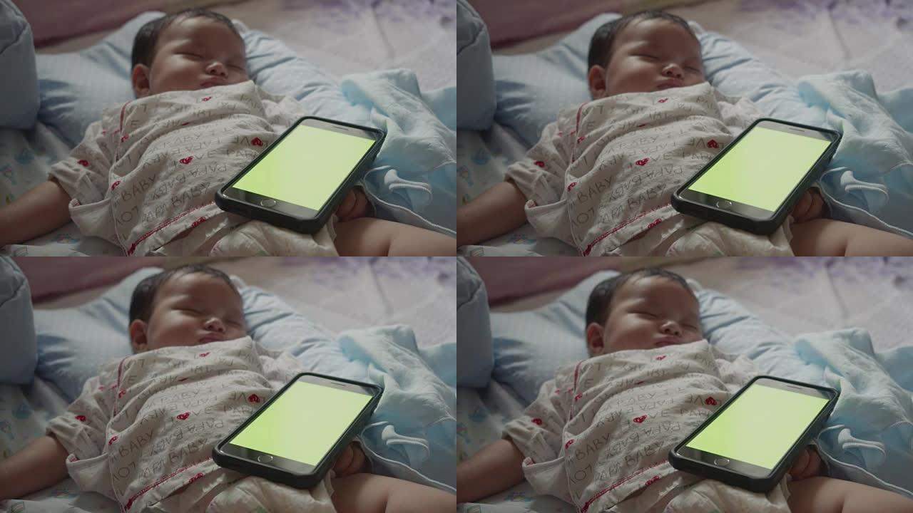 亚洲新生婴儿用绿屏智能手机睡觉