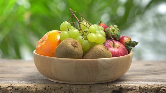 4k混合水果在带有绿色bokeh背景的木碗中。