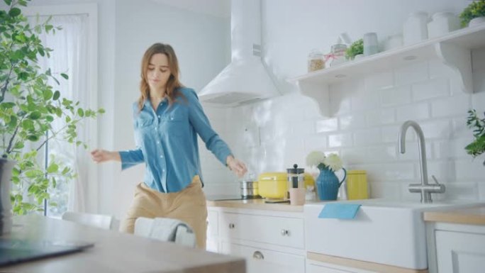 穿着牛仔裤衬衫和棕色裤子的迷人年轻女性正在厨房里创造性地跳舞。阳光现代厨房，拥有健康的生活方式氛围。