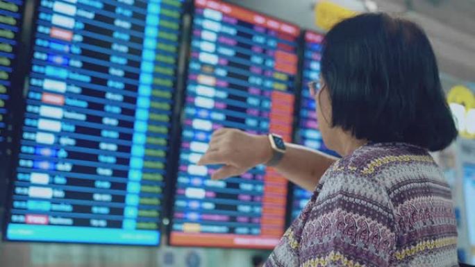 亚洲高级游客在机场用智能手表检查出发板
