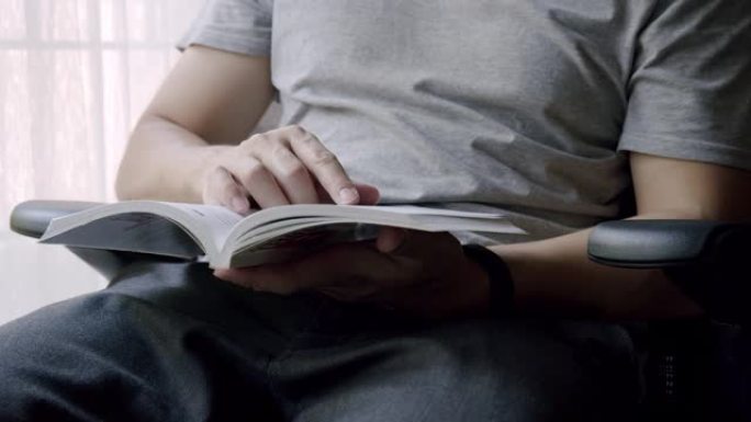 亚洲人呆在家里一边看一本小说。他翻页有趣的学习书。成年男子用手指指着一本书。
