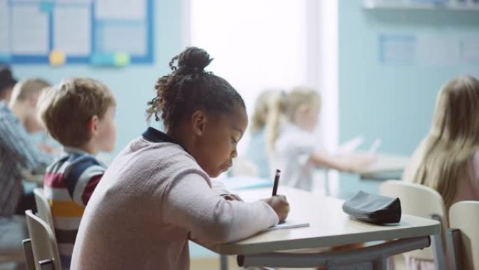 在小学课堂上: 一个戴着牙套的聪明黑人女孩的肖像写在练习笔记本上，微笑。初级教室里有不同群体的聪明孩