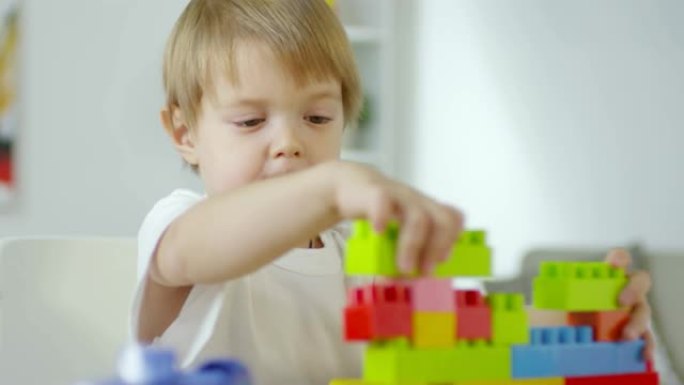 小男孩在餐桌上用彩色砖块制作玩具建筑