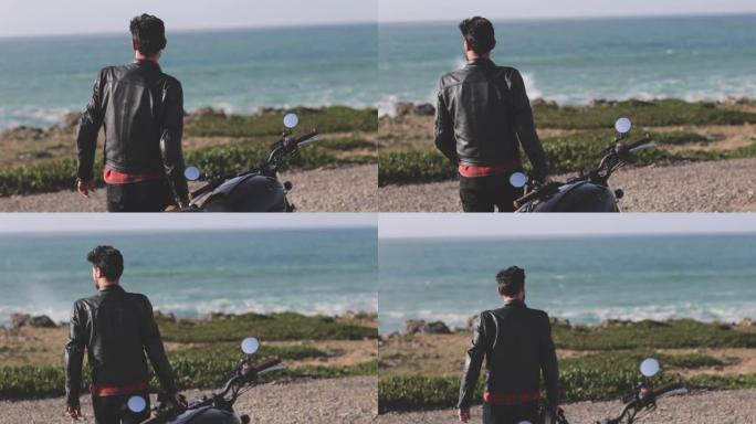 英俊的骑自行车的人从经典摩托车走向海滨