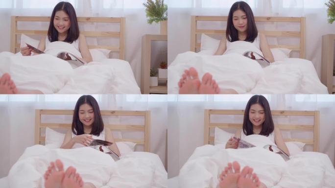 美丽迷人的年轻亚洲女子躺在床上看书，早上在家里的卧室里放松。生活方式女性使用在家放松时间的概念。