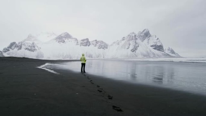 WS女人站在黑沙滩上，看着雪山，冰岛Stokksnes海滩