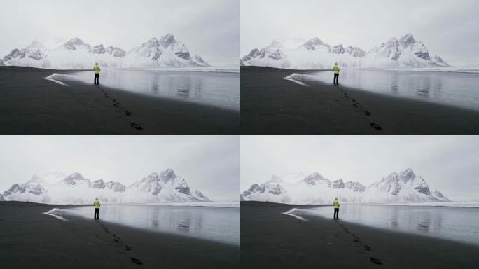 WS女人站在黑沙滩上，看着雪山，冰岛Stokksnes海滩