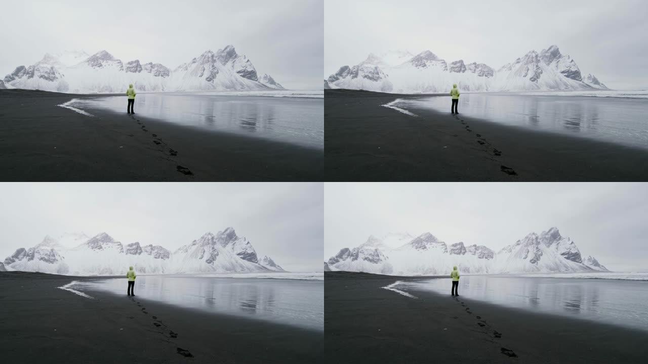 WS女人站在黑沙滩上，看着雪山，冰岛Stokksnes海滩