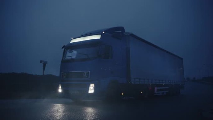 满载货物拖车的长途半卡车在高速公路上行驶。清晨开车穿越大陆，穿过雨，雾。工业仓库区。慢动作拍摄后的正