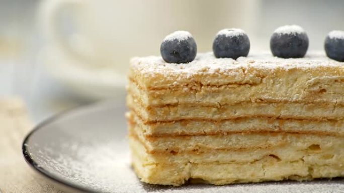 奶油酥皮拿破仑蛋糕，上面覆盖着糖粉，并装饰着四个蓝莓。滑动镜头，4K