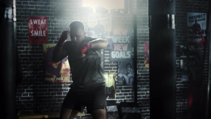强壮英俊的男拳击手正在阁楼健身房锻炼，墙上贴着励志海报。男性运动员正在空中练习拳击。他很认真，精力充