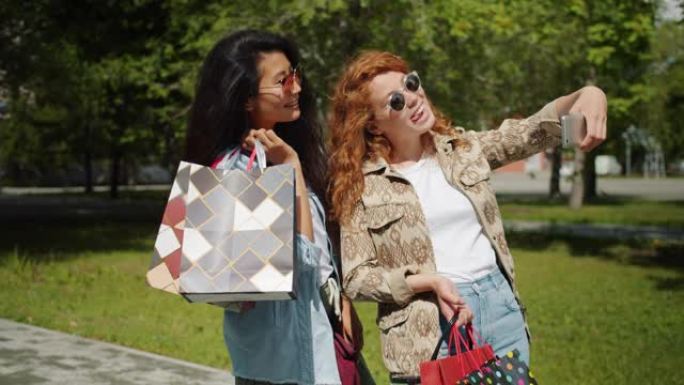 几个女孩在公园里用智能手机拿着购物袋自拍