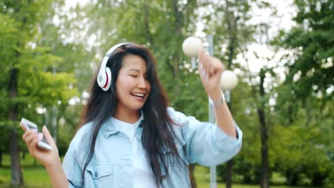 使用智能手机在耳机中户外跳舞的亚洲学生的慢动作