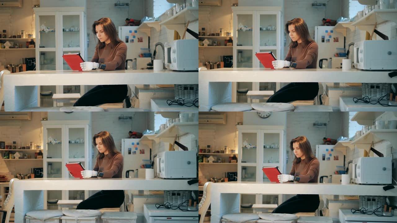 一个用假手的女人正在厨房里用平板电脑工作