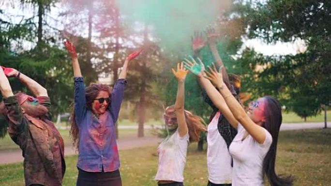在公园户外的胡里节上，快乐的年轻人慢动作跳跃，然后投掷粉末。学生的脸、头发和衣服五颜六色。