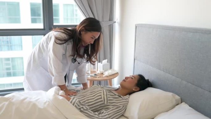 亚洲华裔女性患者躺在床上，女医生正在用听诊器检查她的心跳