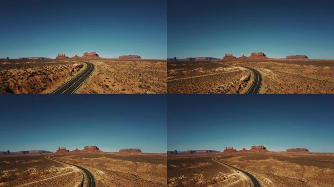 无人机在空旷的沙漠道路上升起，揭示了美国阳光明媚的纪念碑谷令人惊叹的无尽广阔空间。
