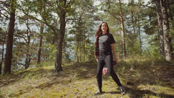 快乐美丽的年轻女子在欧洲松树林中散步和跳舞。这是大自然温暖的晴天。她在阳光下微笑着曲折。树林是绿色和