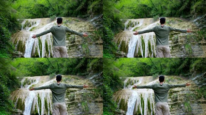 快乐的年轻人，在自己呼吸的空气转化的气，感觉自由和独立，在一个美丽的瀑布和岩石的背景。