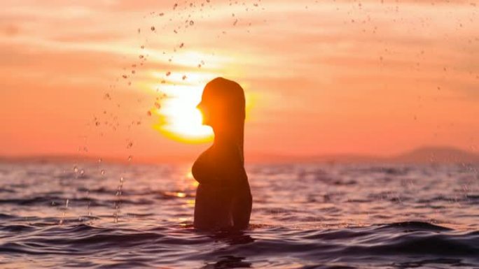 热带度假的女人在日落时分在海洋中泼水长发
