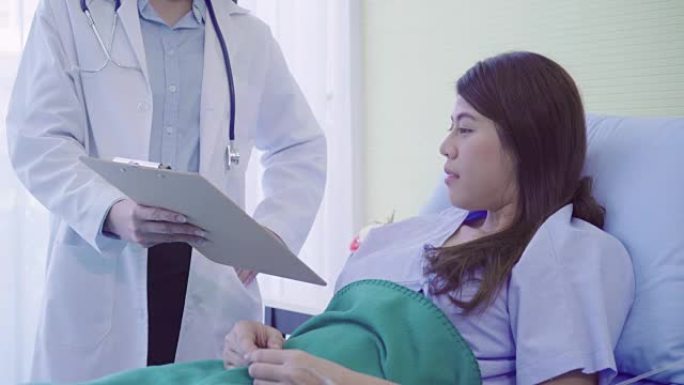 美丽聪明的亚洲医生和病人讨论和解释与医生手中的剪贴板而在病人的病床上在医院。医学保健理念。