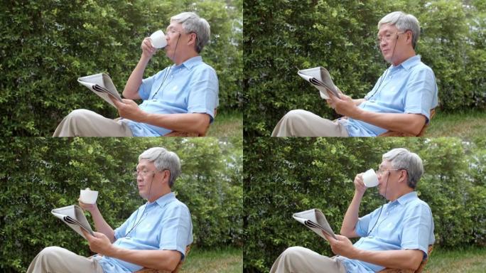 亚洲老人在家放松。亚洲资深中国男性享受休息时间早上在家躺在花园里时戴眼镜看报纸喝咖啡概念。