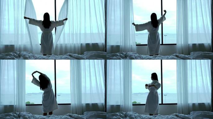 4k镜头场景迷人的亚洲女性的背面早晨醒来，在豪华酒店的卧室里锻炼并看着床上的窗户，生活方式和休闲概念