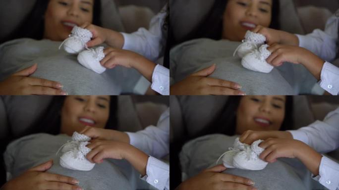 姐姐在母亲怀孕的肚子上玩婴儿鞋的特写镜头