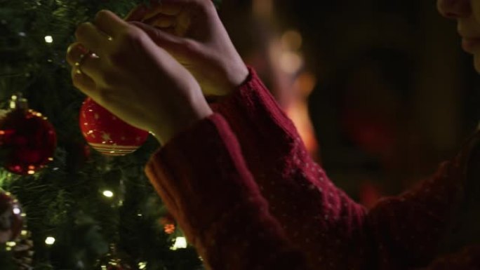 一个年轻女子的慢动作正在用红球装饰圣诞树。