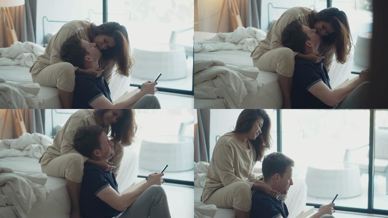 甜蜜的夫妇早上在床上用智能手机拍照。