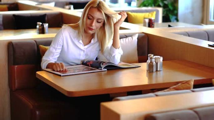 年轻漂亮的女人坐在餐馆或咖啡馆里，看着菜单。