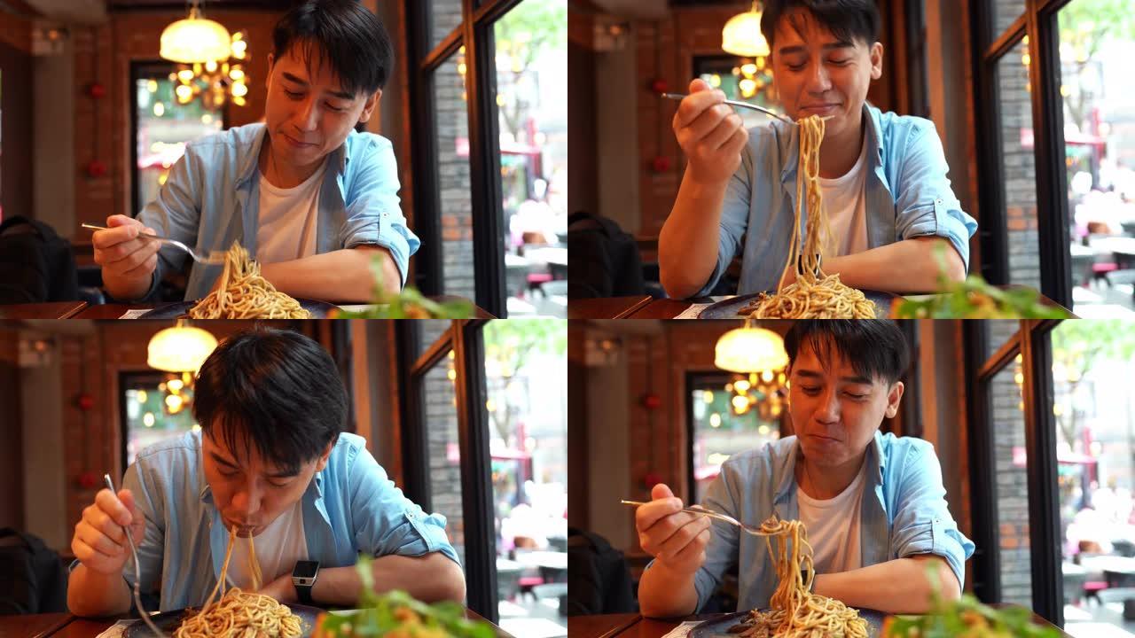 亚洲青年男子一边吃面条一边看手机