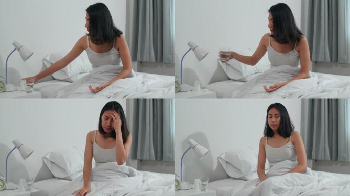 不健康患病的印度女性患有失眠。亚洲年轻女子服用止痛药缓解头痛疼痛，早上坐在家里卧室的床上喝一杯水。