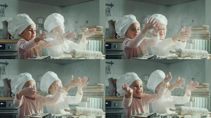 两个漂亮的孩子 (姐妹) 穿着厨师的衣服，在厨房里用面粉做饭和玩耍的肖像。