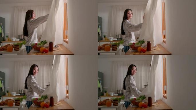 年轻的亚洲迷人的女人在厨房打开窗帘，看着窗户，早上的时候，微笑着，生活方式，自然美丽，感觉在家舒适。