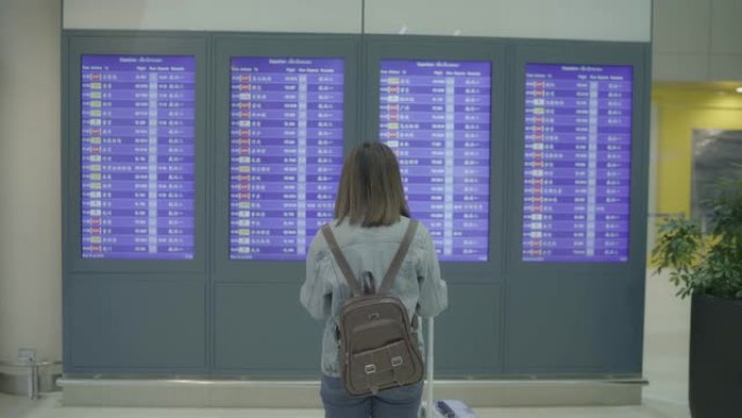 快乐的亚洲女人在国际机场登机口的候机楼大厅看着信息板，用行李检查她的航班。生活方式女性在机场概念中快