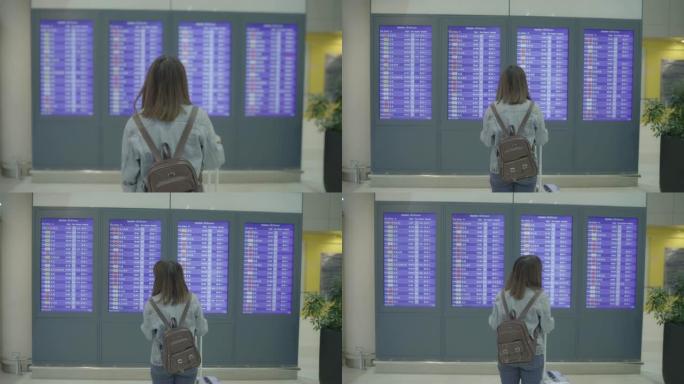 快乐的亚洲女人在国际机场登机口的候机楼大厅看着信息板，用行李检查她的航班。生活方式女性在机场概念中快
