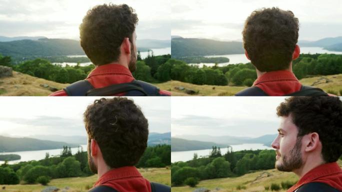 一名年轻的成年白人男子站在山顶上欣赏山景，近距离观看，后视图