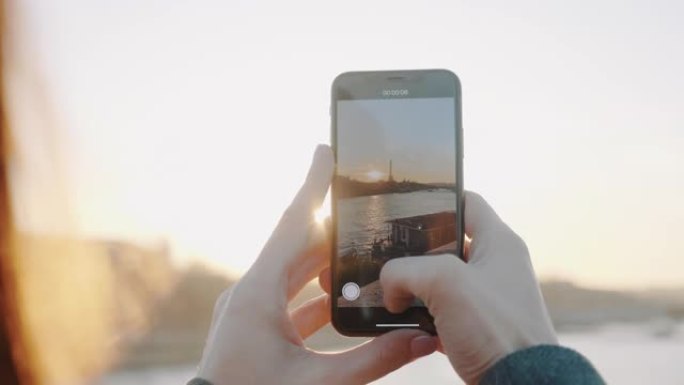 惊人的特写，快乐的女人在巴黎的艾菲尔铁塔和塞纳河拍摄日落的智能手机视频慢动作。