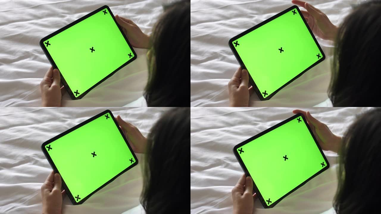 年轻女子躺在床上看着家里绿屏的数字平板电脑，水平