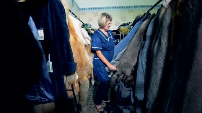 一个女人在房间的衣架上检查动物皮草，关闭。