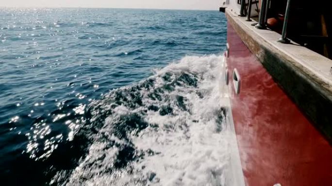 相机在游轮的左侧，在深蓝色的大海中快速航行，在阳光明媚的日子里切割着闪闪发光的白浪。